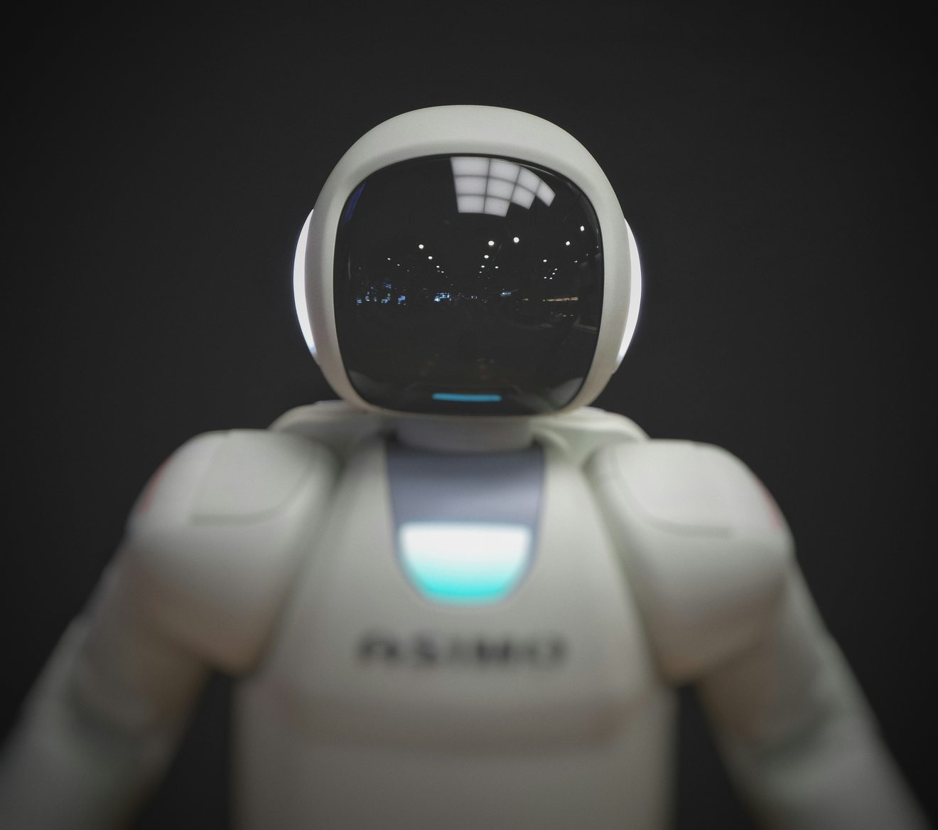 A white humanoid robot with a dark visor and an illuminated blue chest panel against a grey background