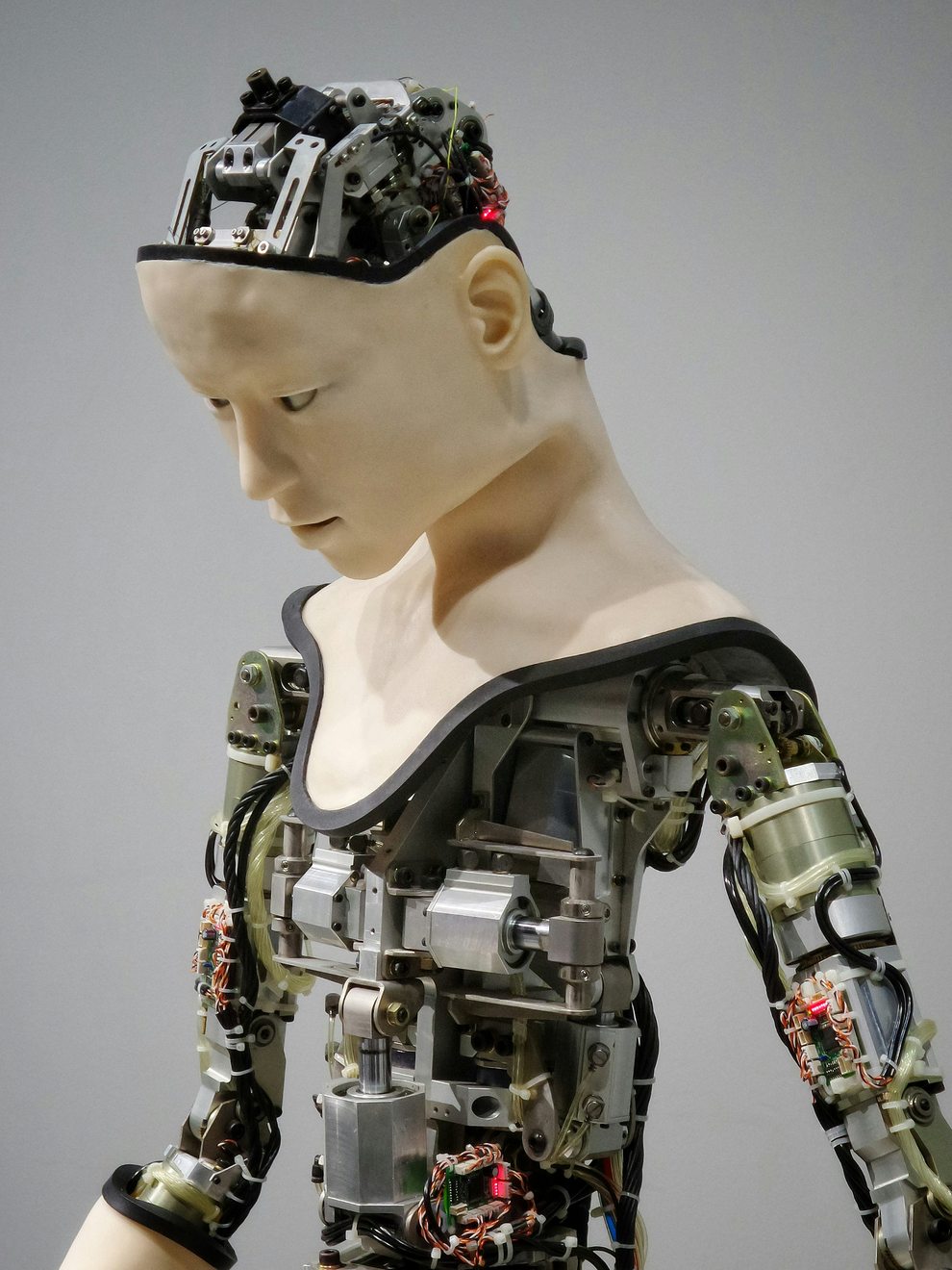 An android figure with a human-like face and exposed mechanical joints, wiring and actuators